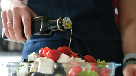 Female Hands Drizzle Oil On Greek Salad. Delicious Vegetarian Mealの写真素材