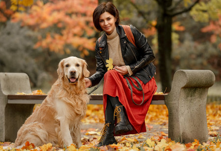 A young woman sitting on a bench in an autumn park and petting a Golden Retriever dogの写真素材