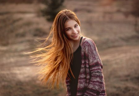 Attractive girl with sun in fluttering hair on nature backgroundの写真素材