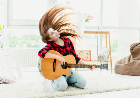 Cute young girl with guitar waving long hair in modern roomの写真素材