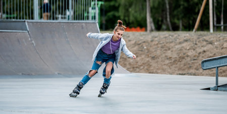 Beautiful girl roller skater riding in city park with ramp. Pretty female teenager rollerskating in casual clothesの写真素材