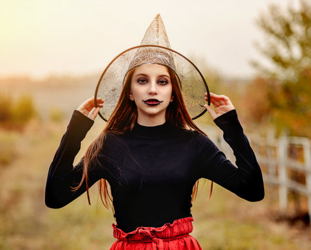 halloween portrait of teenage girl in witch hat smiling at camera on nature backgroundの写真素材