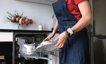 Girl Retrieves Clean Plate From Dishwasher In Close-Up Viewの写真素材