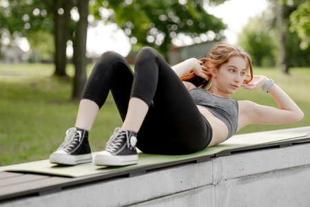 Girl Works Out Abs In Park At Dawn In Summerの写真素材