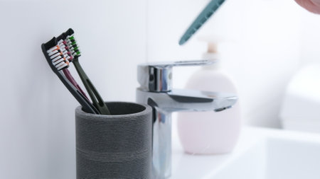 WomanS Hand Throws Toothbrush Into Glass With 4 Toothbrushes Already In Itの写真素材