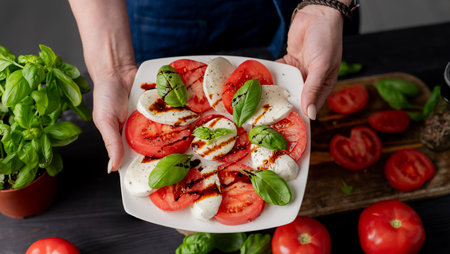 Woman Holds Caprese Salad On Plate, Close-Up Of Tomatoes And Mozzarella Cheeseの写真素材