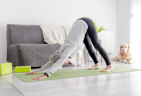 Elderly Woman Practices Downward Dog Yoga Pose At Homeの写真素材
