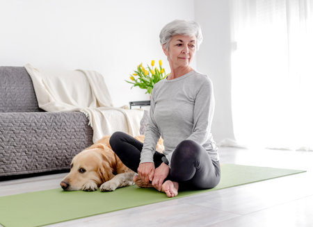 Grey-Haired Retired Woman Practices Yoga At Home Next To Her Golden Retriever Dogの写真素材
