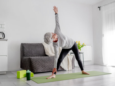 Retired Woman Practices Yoga, Doing Bends At Home In Living Roomの写真素材
