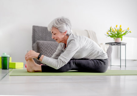 Sporty Lifestyle In Retirement, A Sweet Grey-Haired Woman Exercises On The Living Room Floorの写真素材