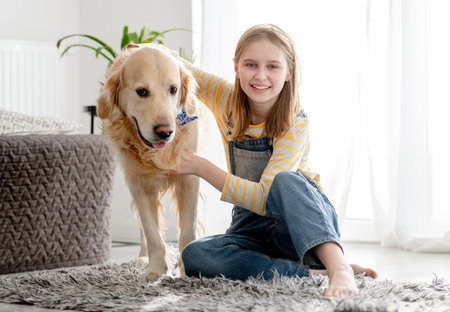 Girl With Golden Retriever Sits On Floor In Room Playing With Dogの写真素材