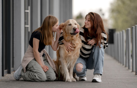 Two Girls With Golden Retriever Sitting And Playing Outside In Springの写真素材