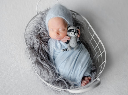 Newborn Baby In Grey Wrap Sleeps In Metal Basket During Studio Photoshootの写真素材
