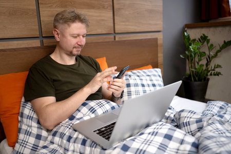 In The Morning, A Man Lying In Bed With A Laptop And Smartphone At Homeの写真素材