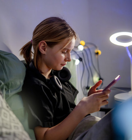 Cute Little Girl Chatting On Social Media With Smartphone In Bed Before Sleepの写真素材