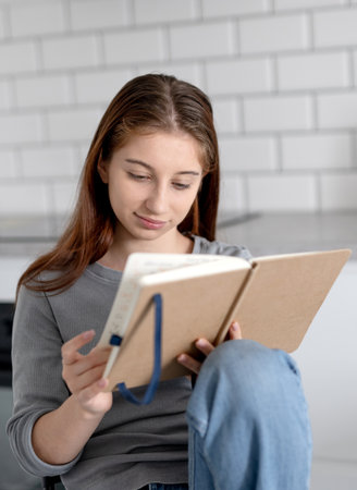Sweet Teen Girl Reading Notebook Entries While Sitting On A Chair At Home
