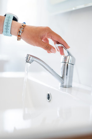 Womans Hand Turning On The Faucet Water In The Bathroom At Homeの写真素材