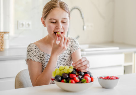 Happy Teenage Girl Eating Grapes At The Kitchen Table At Homeの写真素材