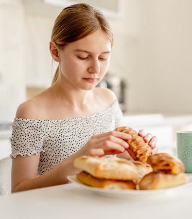 Happy Teenage Girl Eating Pastry In The Kitchen At Homeの写真素材