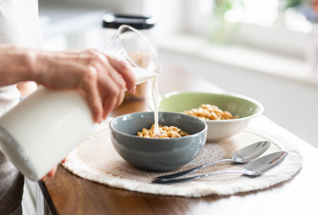 Woman Pouring Milk Into Cereal At Home In The Kitchen Close-Upの写真素材