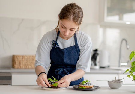 Girl Decorates Dessert With Mint Leaves And Blueberries At Home In The Kitchenの写真素材