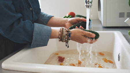 Woman Washing Cucumbers Over The Kitchen Sinkの写真素材