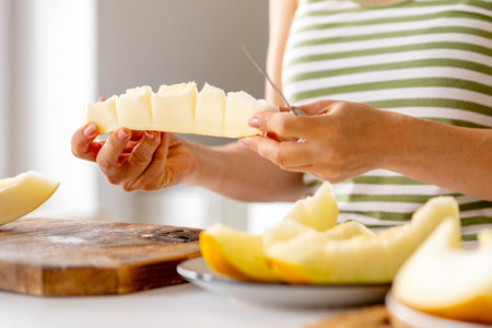 Woman Cutting Melon Into Pieces In The Kitchen Close-Upの写真素材