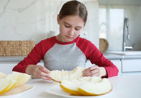 Teen Girl Eating Melon Sitting At The Kitchen Tableの写真素材