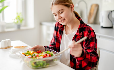 Happy Girl Serving Herself Salad At Home In The Kitchenの写真素材