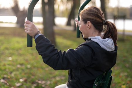 Woman Doing Arm Exercises On Outdoor Gym Equipment In The Park Viewed From Behind
