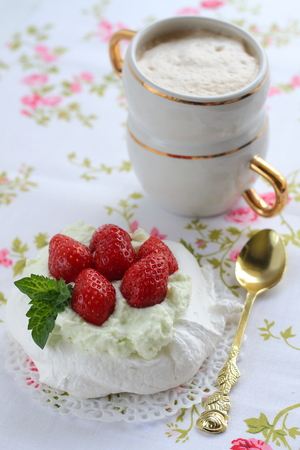 Pavlova cake with strawberries with a cup of cappuccino on a colorful napkinの写真素材