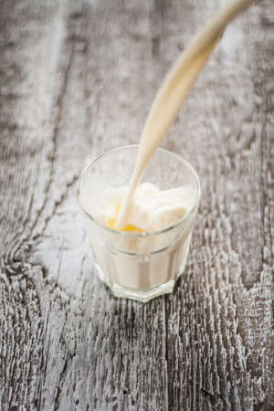 Milk is poured into a glass on a wooden background.