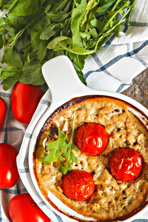 Casserole with zucchini, tomatoes and greens on a napkin on a wooden table.の写真素材