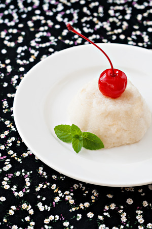 air white mousse dessert on a plate decorated with a cherry and mint on a black background with hearts.の写真素材