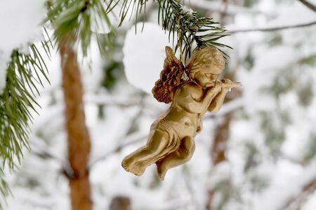 golden angel hangs toy on a snowy branch.の写真素材