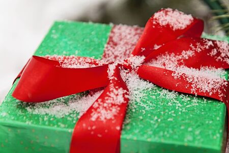Green gift box with a red ribbon sprinkled with snow close-up.の写真素材