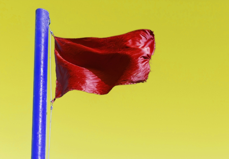 Red flag on the flagpole blue on a yellow background.の写真素材