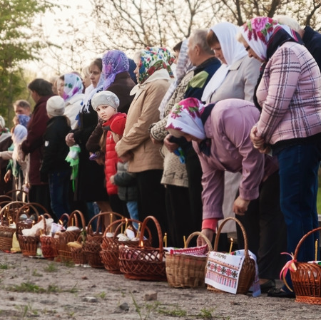 At Easter many people standing in a row with baskets and candles, waiting for the priest to bless....