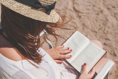 Young adult woman with a hat on the beach reading a book.の写真素材