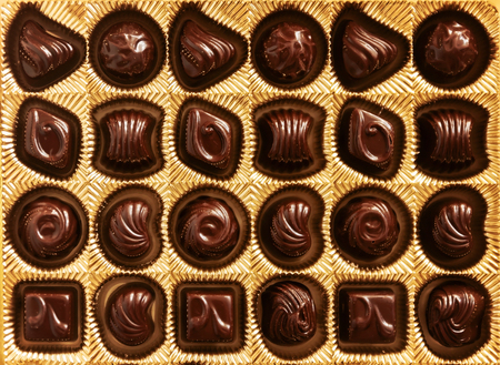 Chocolate candies of different shapes in a gold box, top view, smooth symmetrical rows for...