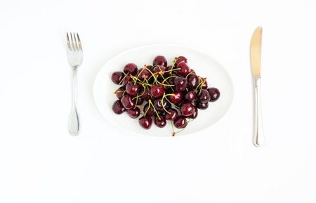Fresh juicy cherry berries on white plate, served with cutlery, isolated on white backgroundの写真素材