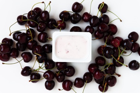 Container with yogurt and a bunch of fresh cherry berries on white background, isolated, top view.の写真素材