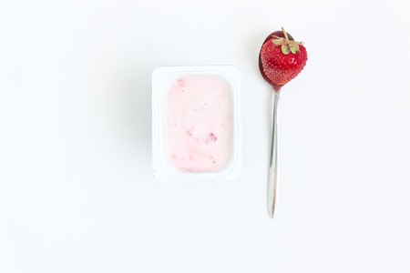 Container with strawberry yogurt and a spoon with one strawberry, top view, isolated on a white background.の写真素材