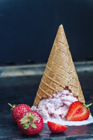 Strawberry ice cream in a waffle cone inverted and melted against a dark background, close-up.の写真素材
