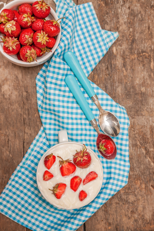 In a cup of yogurt and fresh strawberries, on a blue spoon towel, scattered strawberries, on a wooden background. Close-up, top view.Concept healthy and healthy breakfast.の写真素材