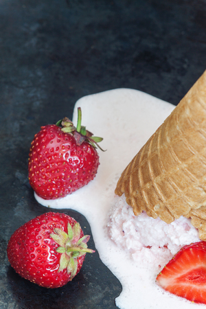 Strawberry ice cream in a waffle cone inverted and melted against a dark background, close-up.の写真素材