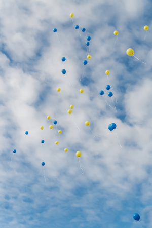 Multicolored balloons fly in clear blue sky with clouds.の写真素材