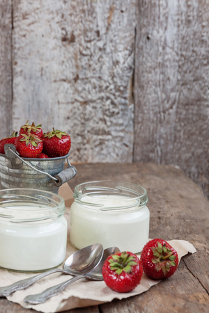 yoghurt in a glass and a bucket with fresh strawberries on a wooden background.の写真素材