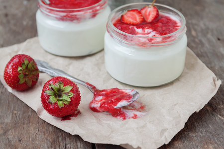 Yogurt with jam sauce in glass and a bucket of fresh strawberries on a wooden background.の写真素材
