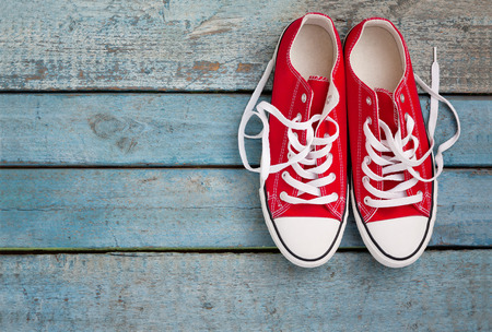Red retro sneakers with loose braids on a blue wooden background.の写真素材